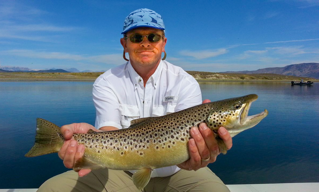 A fly angler holding a trophy 8 lb brown trout from Crowley Lake.
