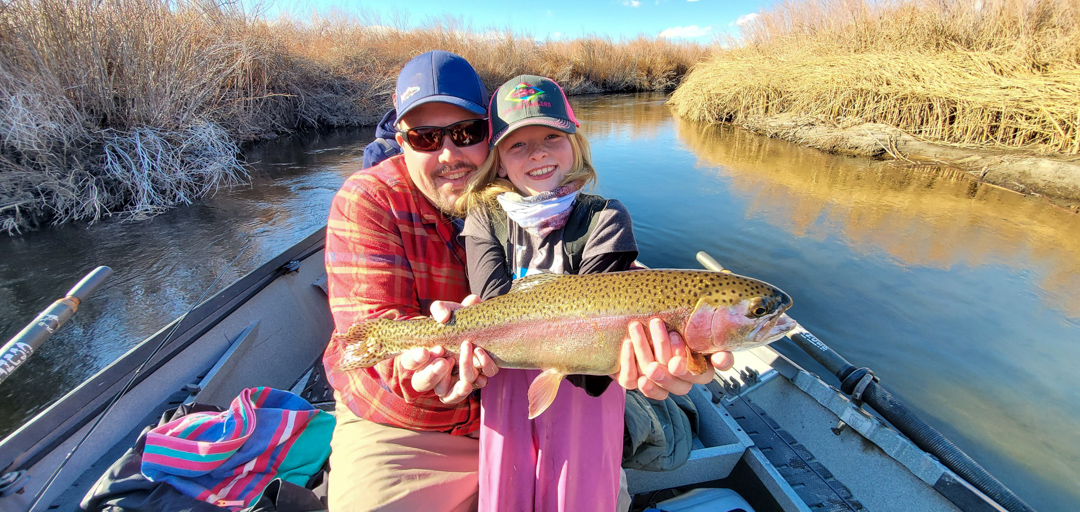A father with his young daughter who is holding a giant rainbow trout in a drift boat on the Lower Owens River.