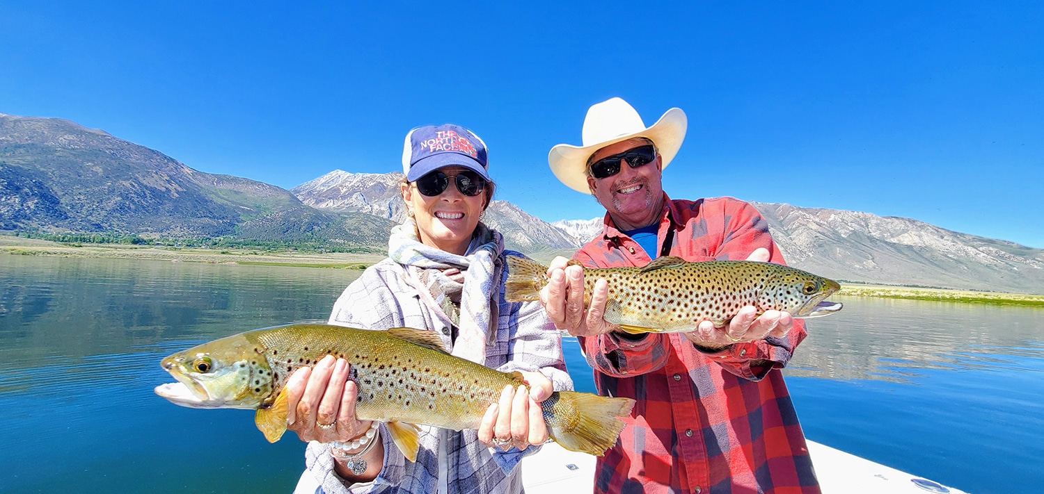 A husband and wife holding a pair of brown trout from Crowley Lake while fishing with an Eastern Sierra Fishing Guide with a view of Mammoth Mountain in the background.