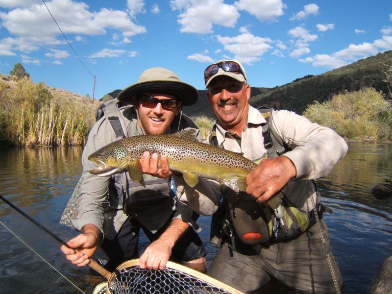 Two fisherman standing in a river holding a large brown trout.