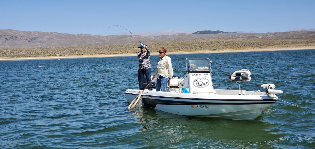 Sierra Drifters Guide Jerry Gilpin assists a fly fisherman in landing a trout from Crowley Lake on a boat.