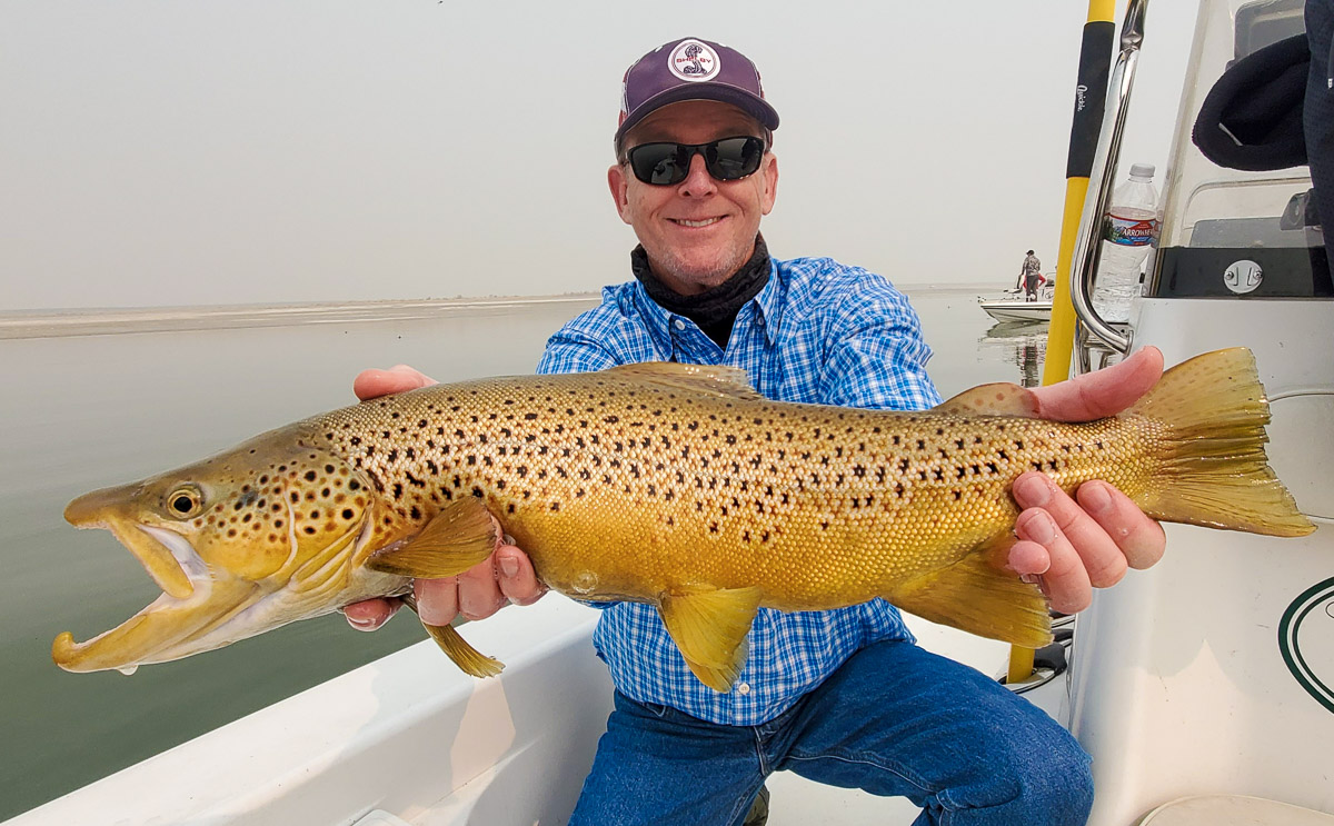 A smiling angler holding a large brown trout from Crowley Lake from a boat.