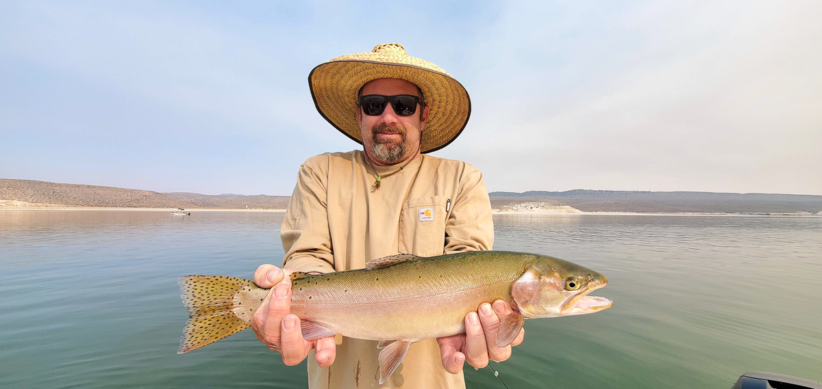 A fly fisherman with a wide brim straw hat holding a cutthroat trout from Crowley Lake.