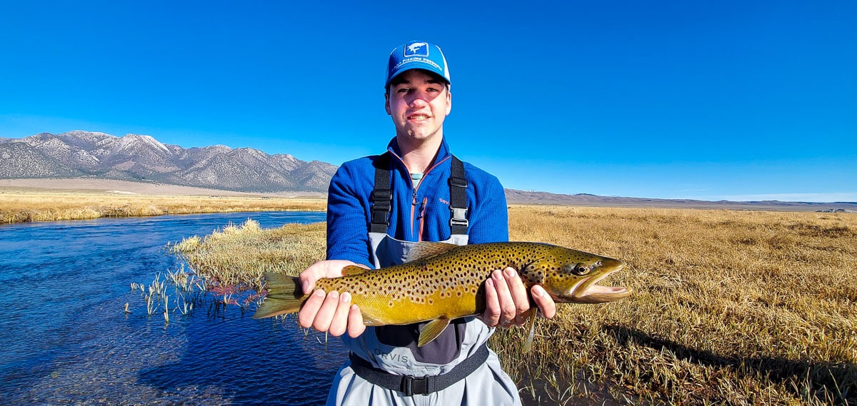 A fly fisherman holding a large brown trout in spawning colors in the fall while standing in the Upper Owens River.