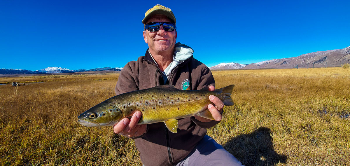A smiling angler holding a brown trout in spawning colors from the Upper Owens River in the fall.