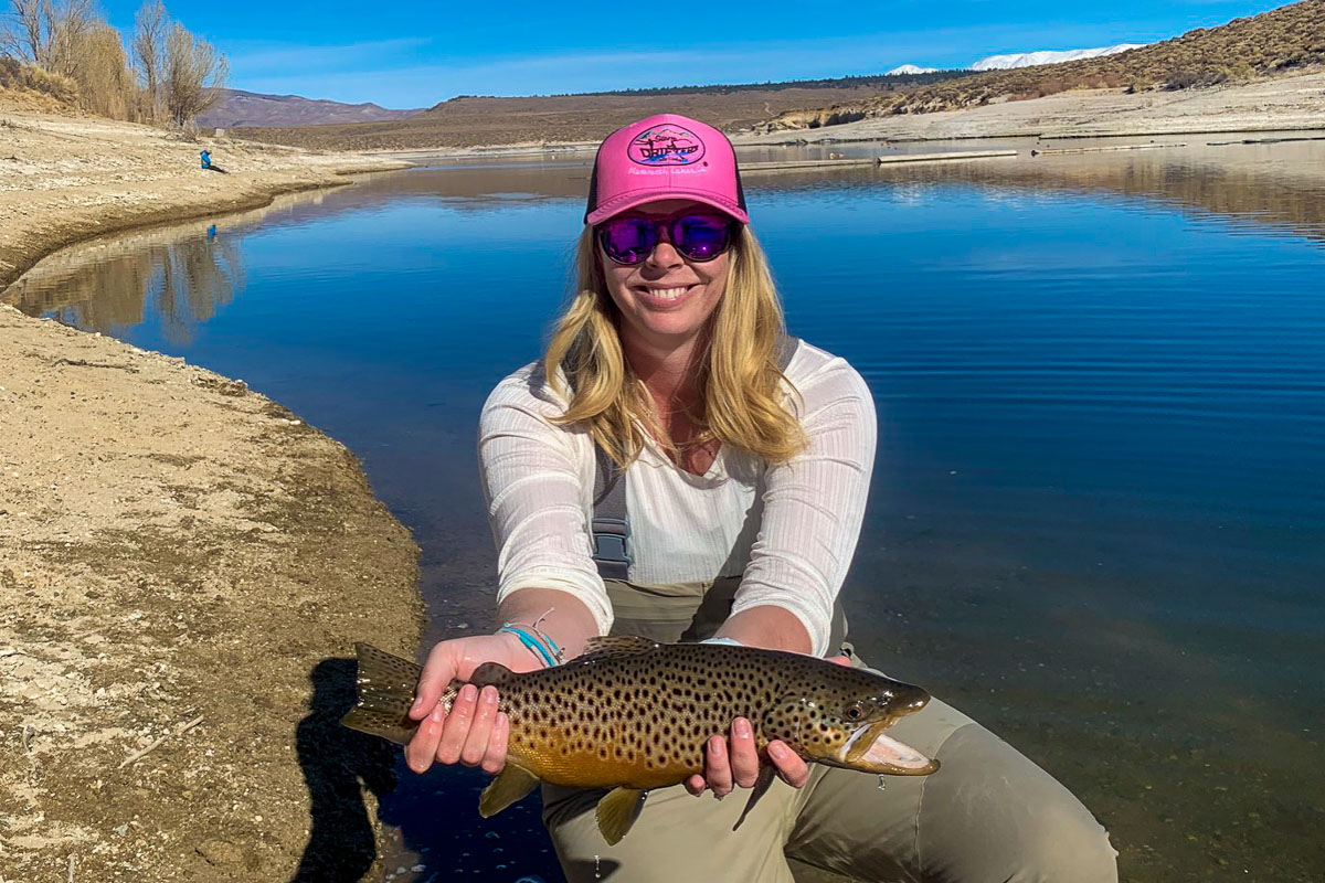 A lady fly fisher holds a brown trout in spawning coloration from Crowley Lake in the fall.