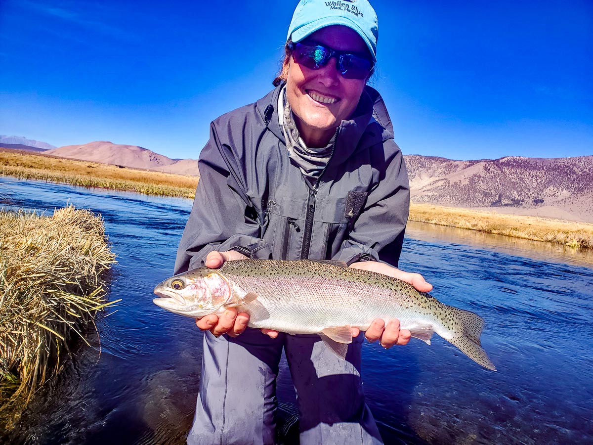 A fly fisherwoman dispays a large rainbow trout while standing in the Upper Owens River.