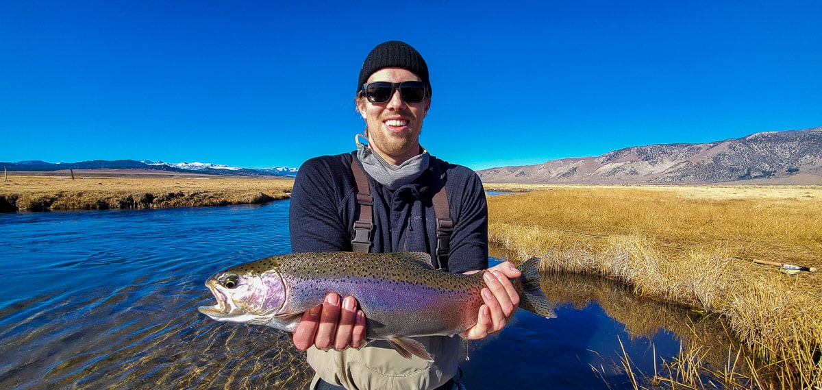 A masked fly fisherman holding a rainbow trout in spawning colors from the Upper Owens River.