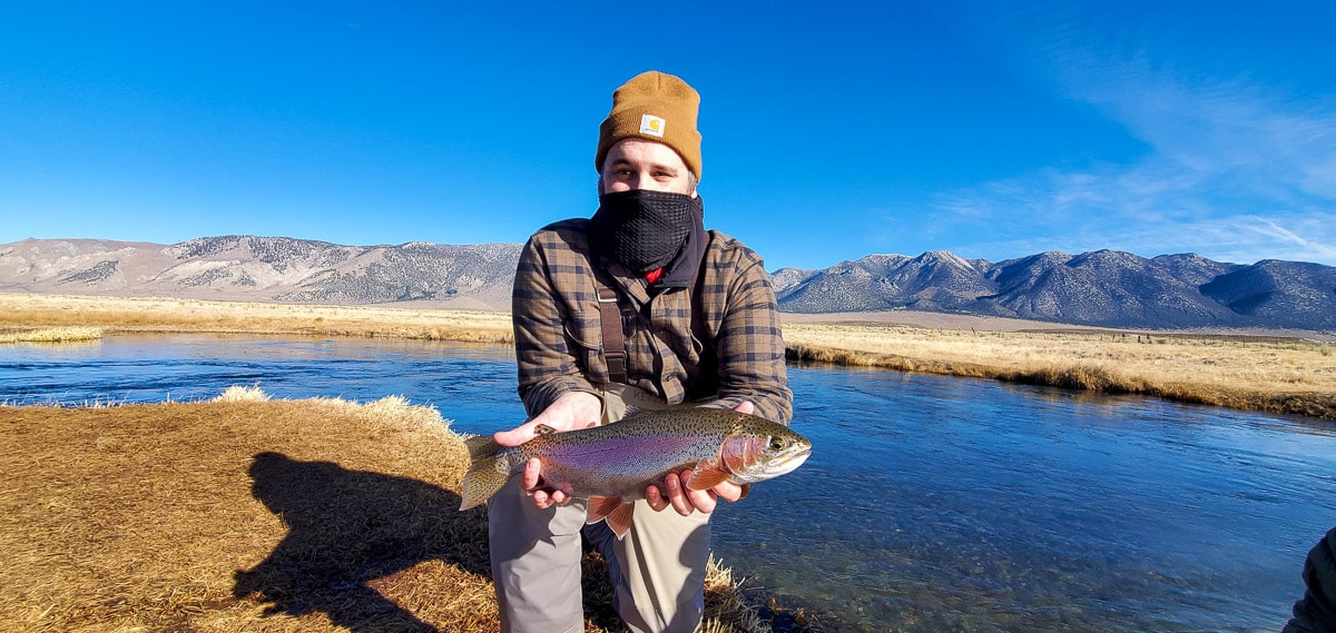 A masked fly fisherman holding a rainbow trout in spawning colors from the Upper Owens River.