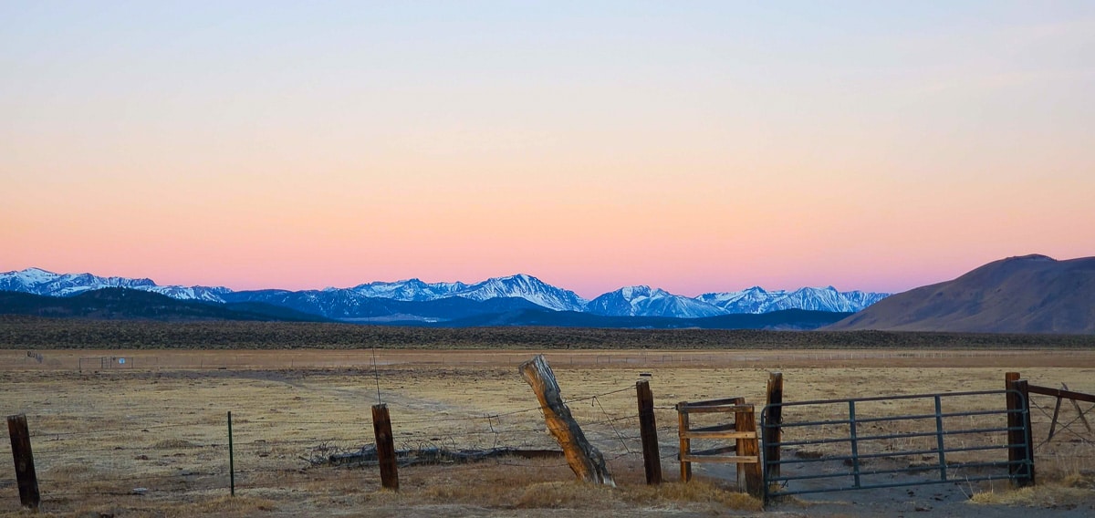 A cold morning before sunrise on the Upper Owens River with a cattle fence in the foreground and snowcapped mountains in the background.