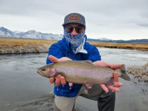 A masked fly fisherman holding a rainbow trout in spawning colors from the Upper Owens River.