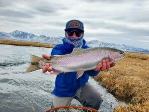 A masked fly fisherman holding a rainbow trout in spawning colors from the Upper Owens River.