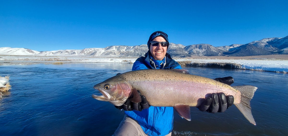 A fly fisherman holding a rainbow trout in spawning colors from the Upper Owens River in the snow.