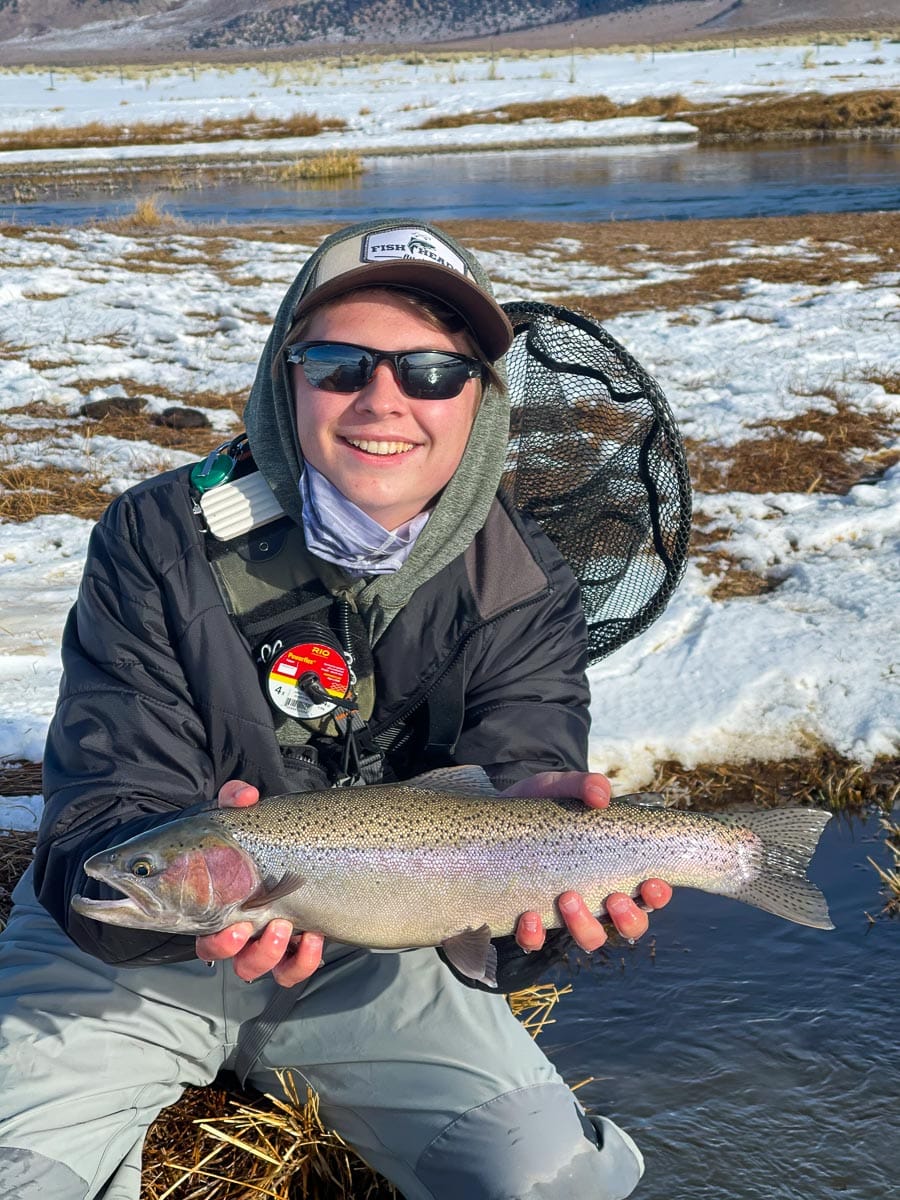 A fly fisherman holding a rainbow trout in spawning colors from the Upper Owens River in the snow.