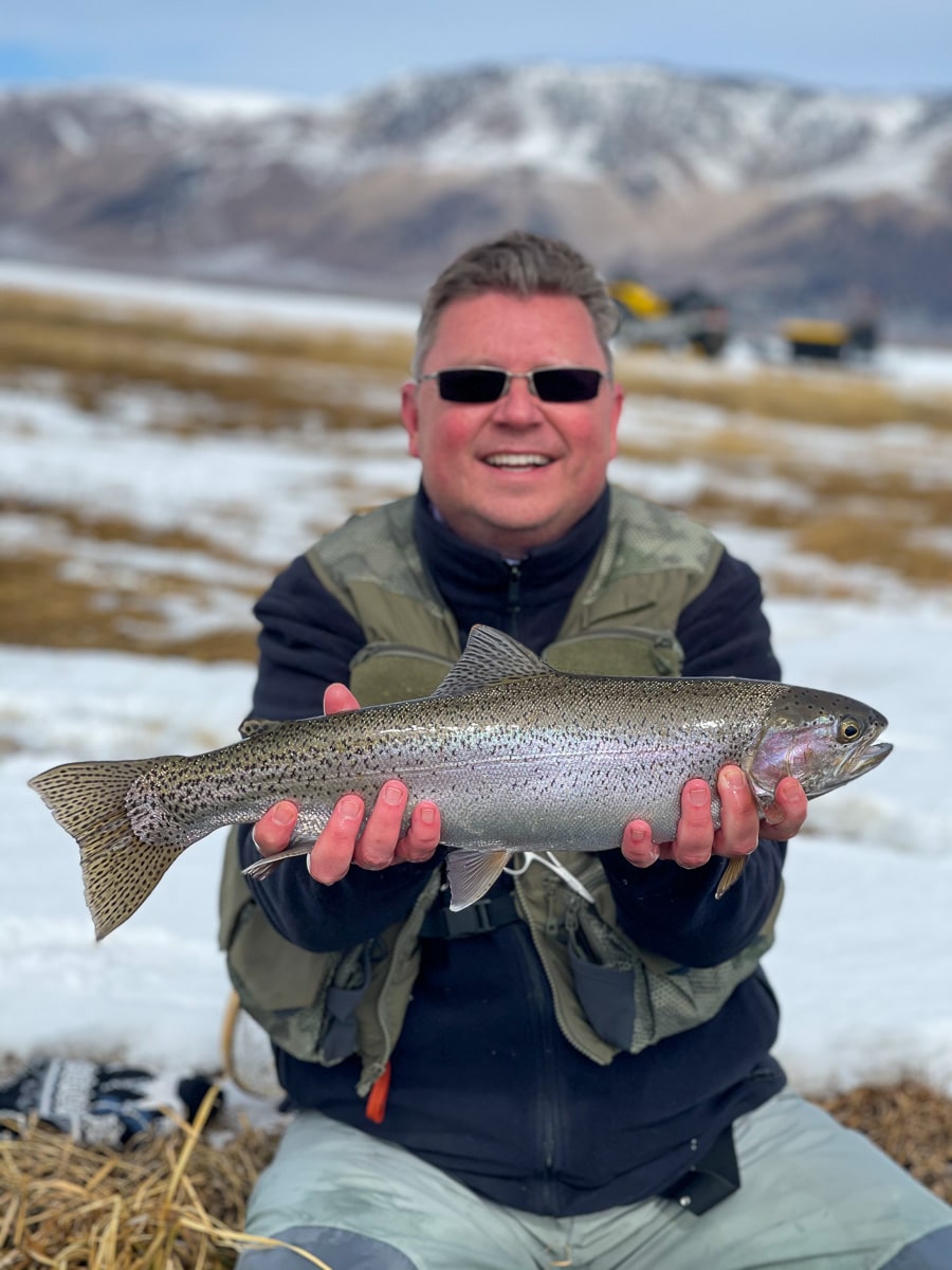 A fly fisherman holding a rainbow trout in spawning colors from the Upper Owens River in the snow.