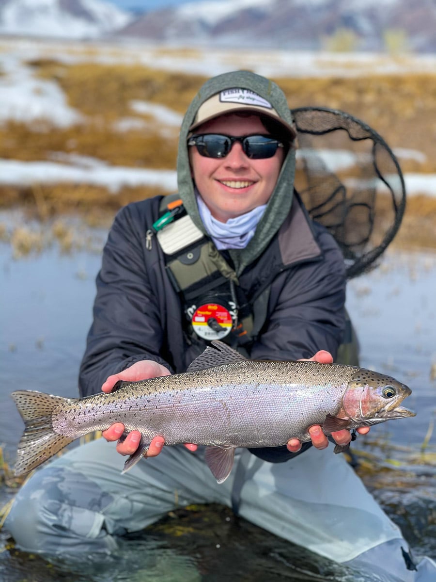 A fly fisherman holding a rainbow trout in spawning colors from the Upper Owens River in the snow.