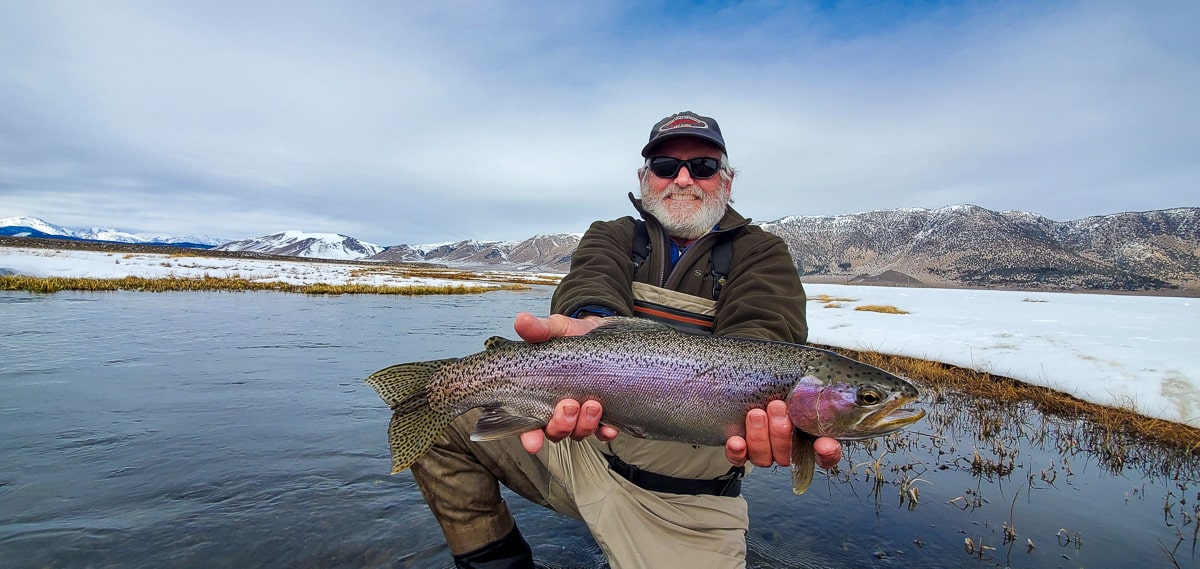 A fly fisherman holding a rainbow trout in spawning colors from the Upper Owens River in the snow.