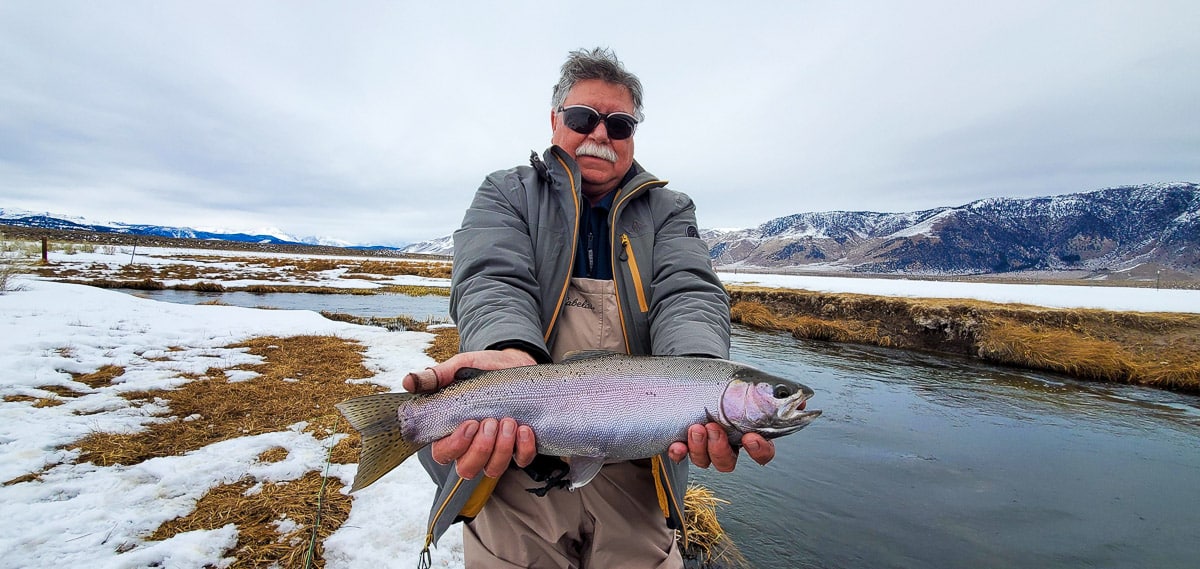 A fly fisherman holding a rainbow trout in spawning colors from the Upper Owens River in the snow.