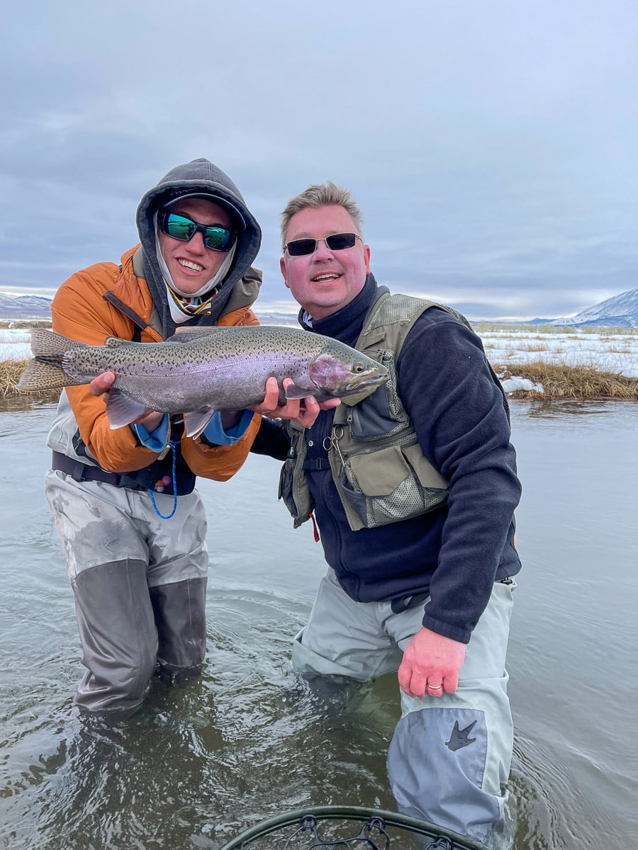 A fly fisherman holding a rainbow trout in spawning colors from the Upper Owens River in the snow.