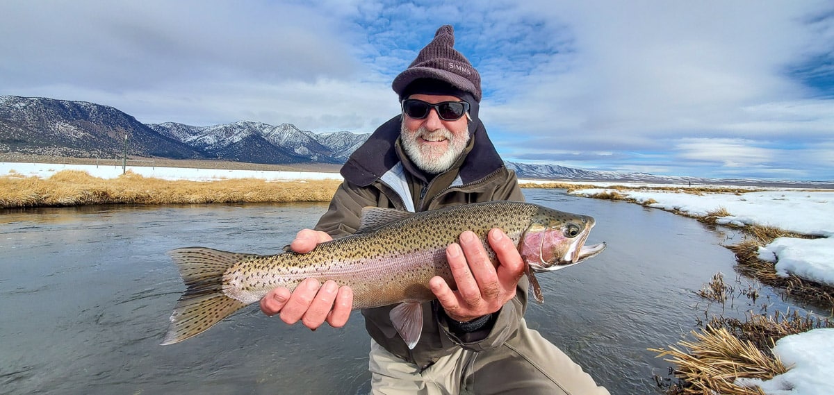 A fly fisherman holding a rainbow trout in spawning colors from the Upper Owens River in the snow.