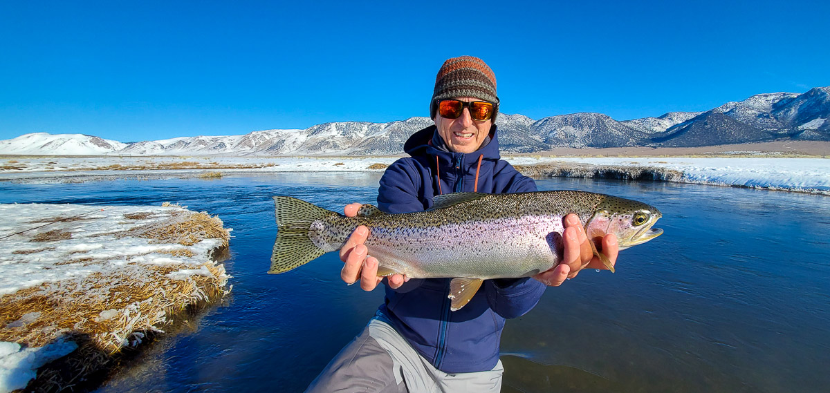 A fly fisherman holding a rainbow trout in spawning colors from the Upper Owens River in the snow.