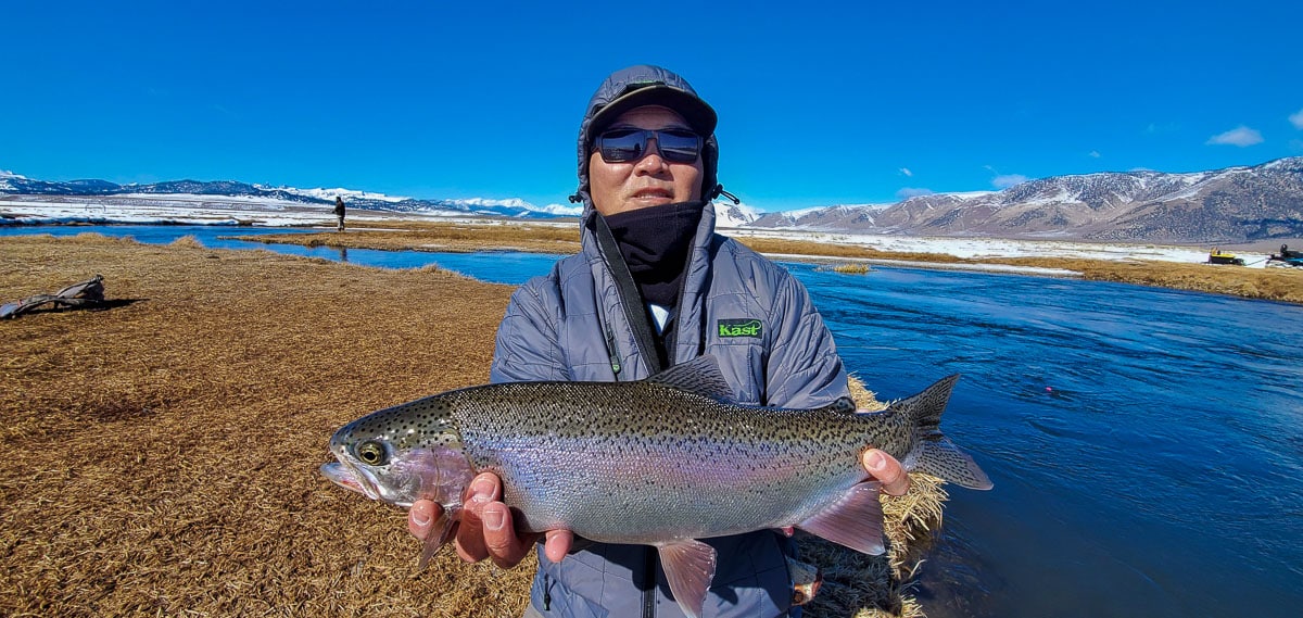 A fly fisherman holding a rainbow trout in spawning colors from the Upper Owens River in the snow.