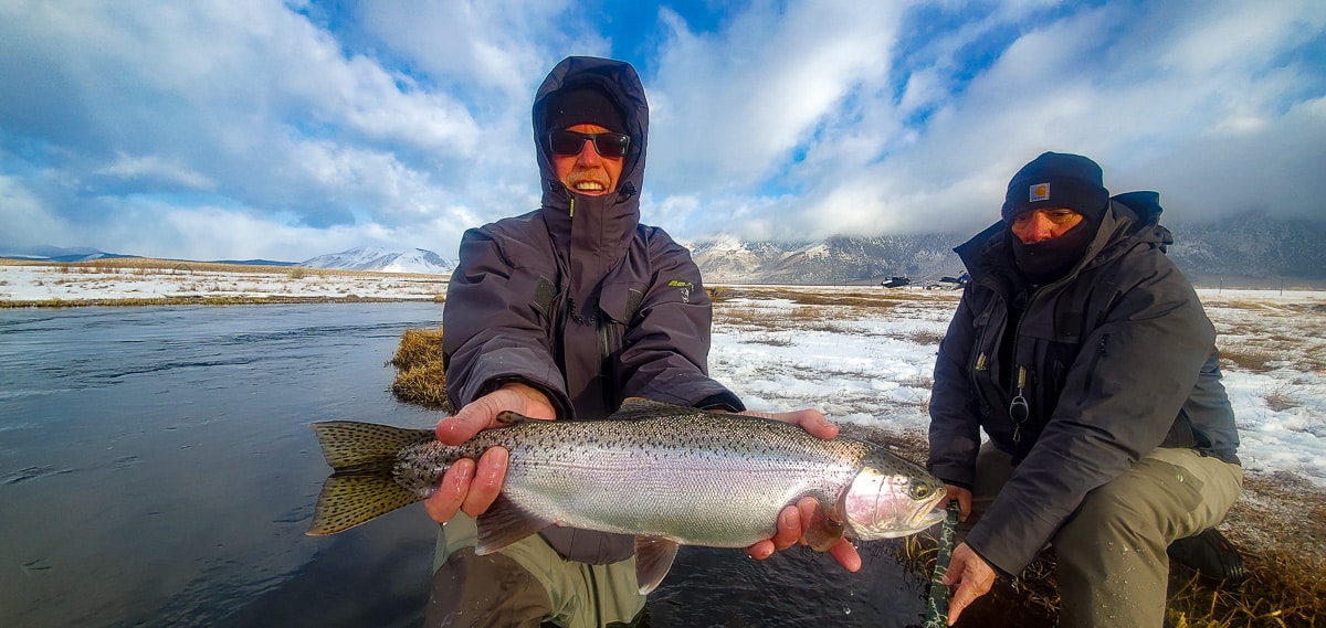 A fly fisherman holding a rainbow trout in spawning colors from the Upper Owens River in the snow.