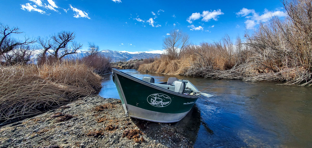 A drift boat resting on a river bank on the Lower Owens River.