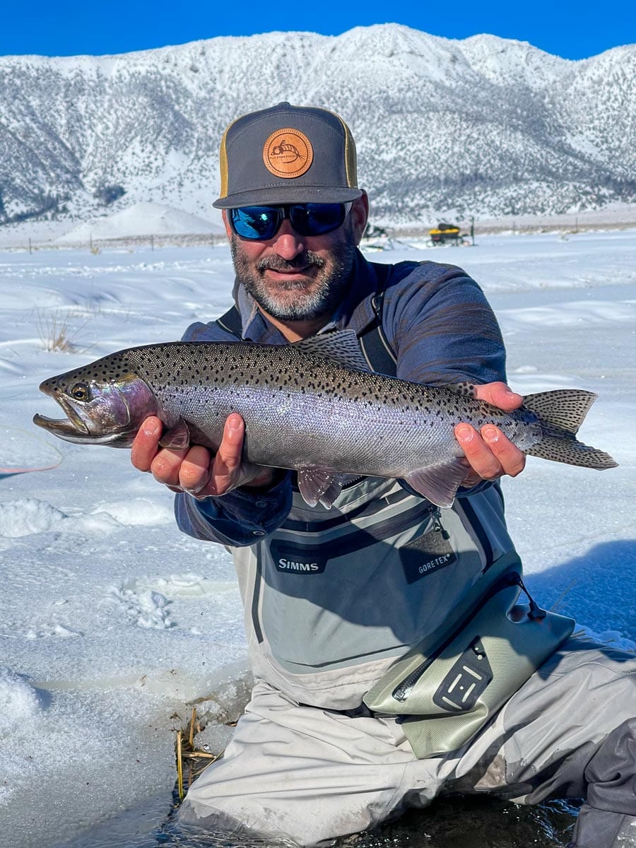 A masked fly fisherman holding a rainbow trout in spawning colors from the Upper Owens River.