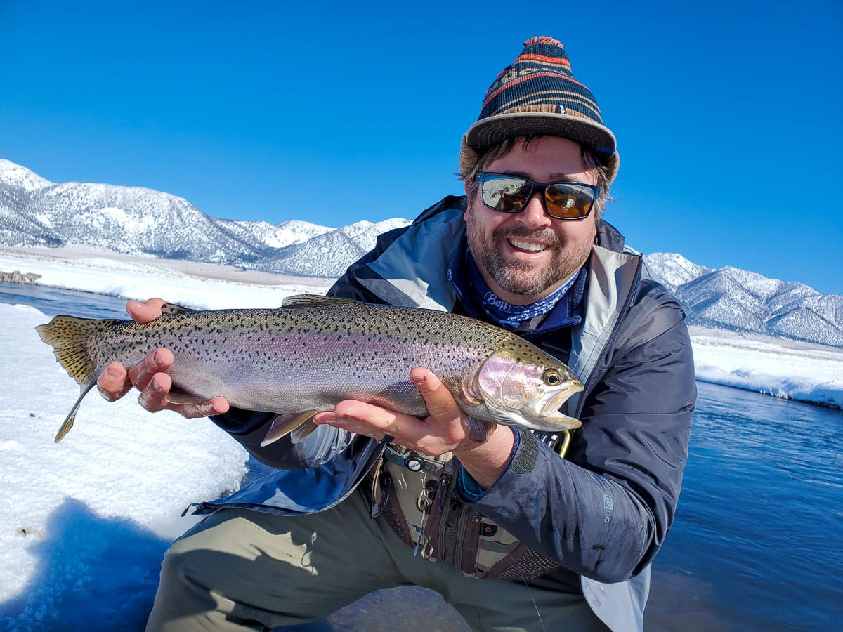 A masked fly fisherman holding a rainbow trout in spawning colors from the Upper Owens River.