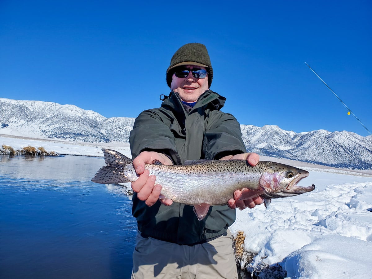 A masked fly fisherman holding a rainbow trout in spawning colors from the Upper Owens River.