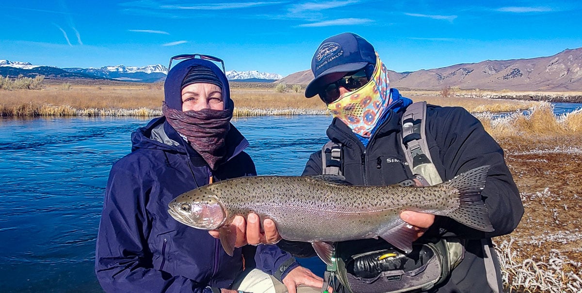 A masked fly fisherman holding a rainbow trout in spawning colors from the Upper Owens River.