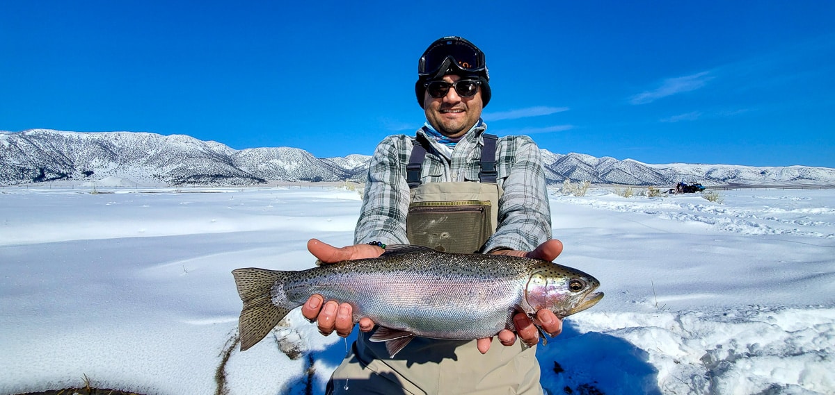 A masked fly fisherman holding a rainbow trout in spawning colors from the Upper Owens River.