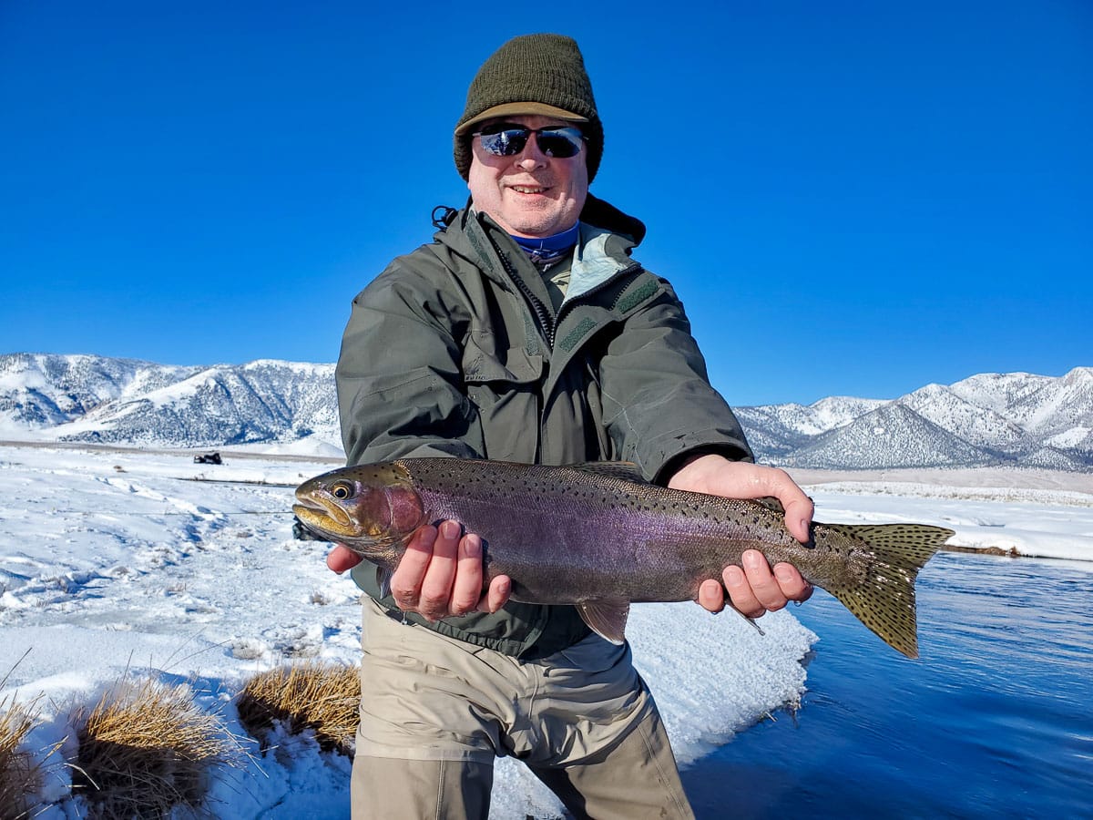 A masked fly fisherman holding a rainbow trout in spawning colors from the Upper Owens River.