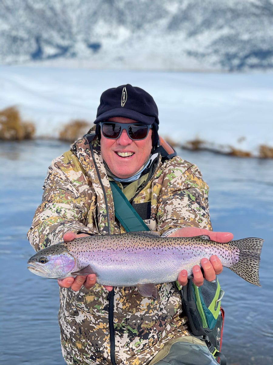 A masked fly fisherman holding a rainbow trout in spawning colors from the Upper Owens River.