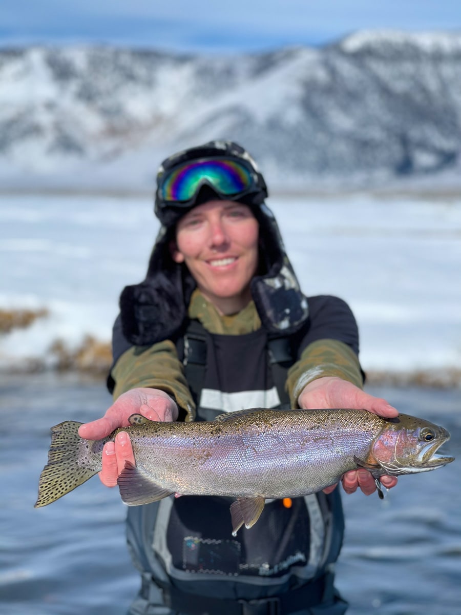 A masked fly fisherman holding a rainbow trout in spawning colors from the Upper Owens River.