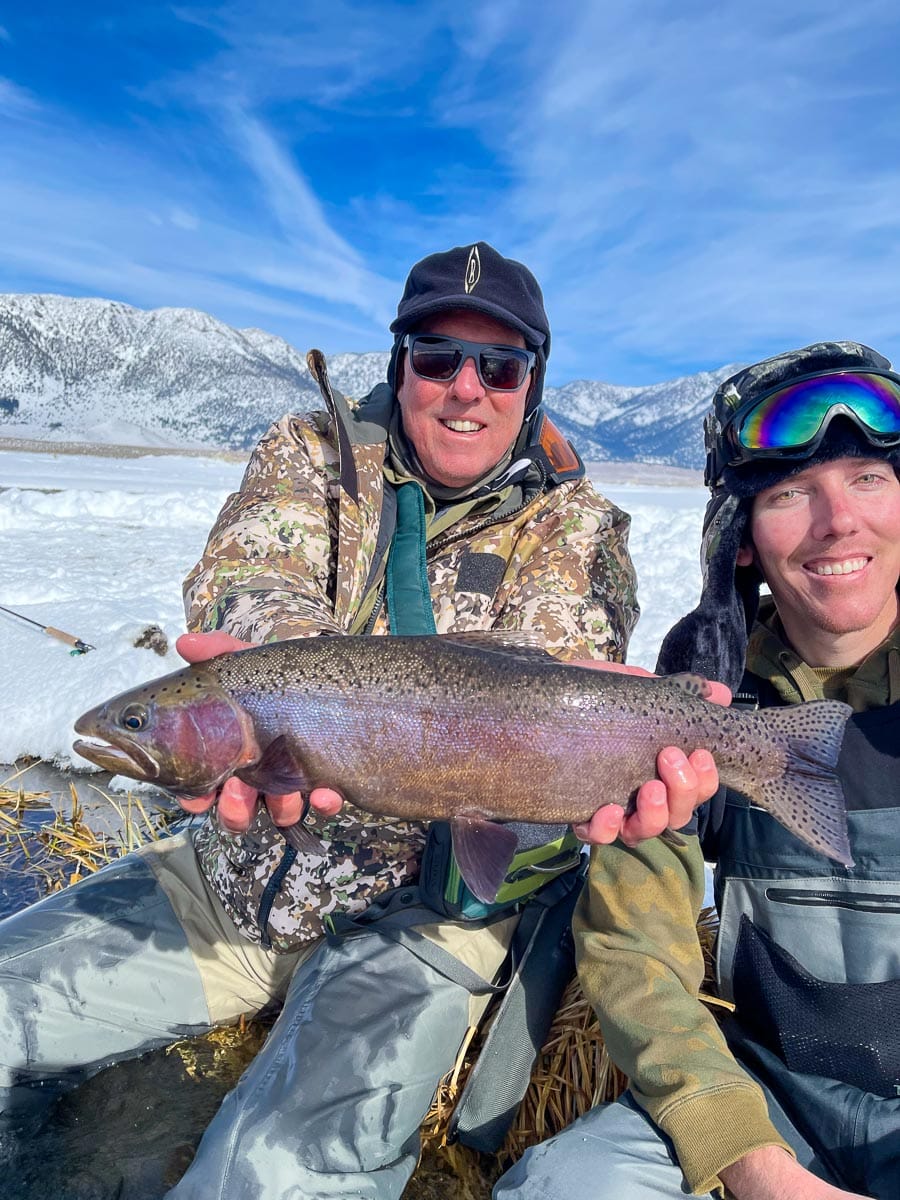 A masked fly fisherman holding a rainbow trout in spawning colors from the Upper Owens River.