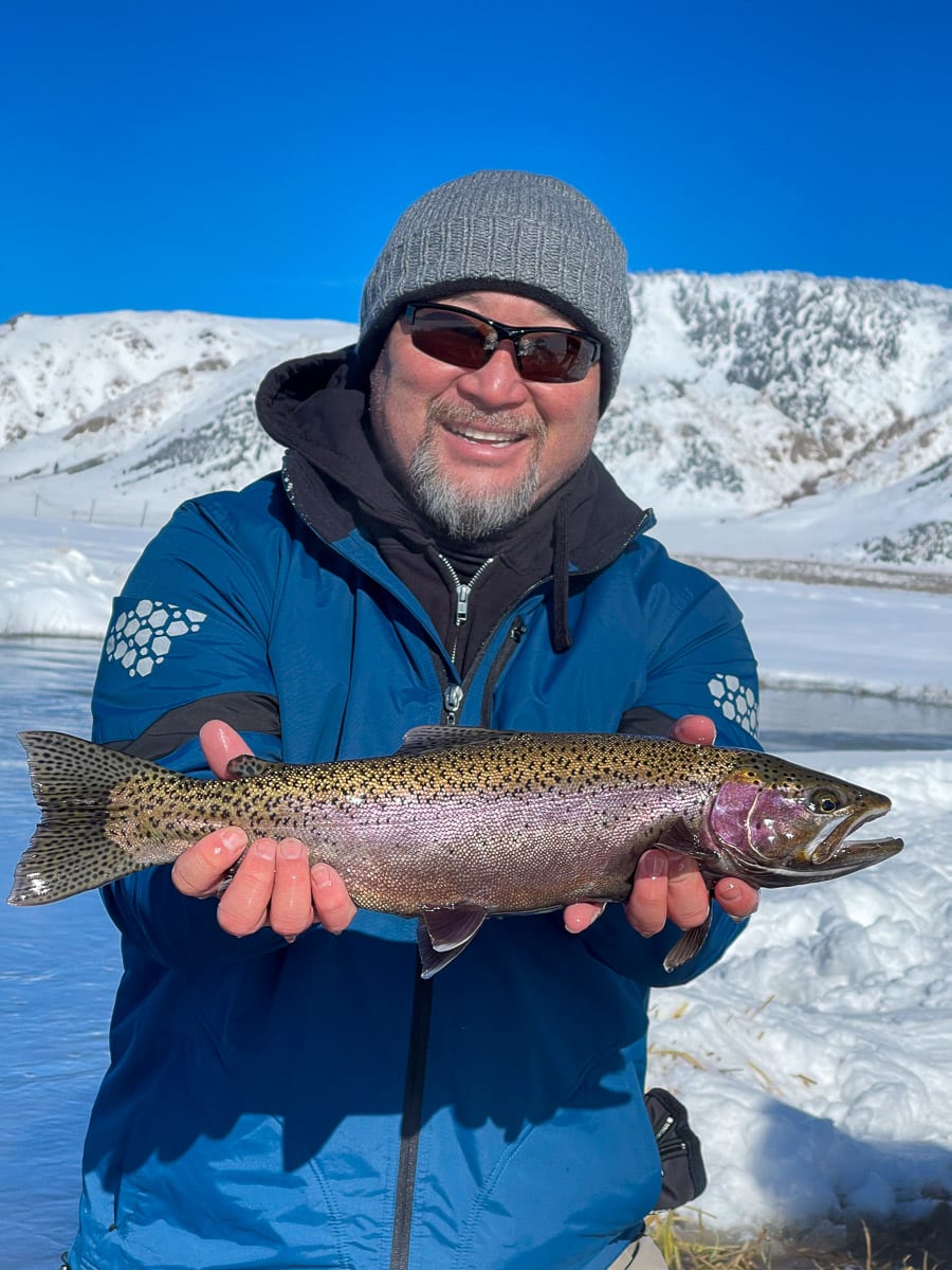 A masked fly fisherman holding a rainbow trout in spawning colors from the Upper Owens River.