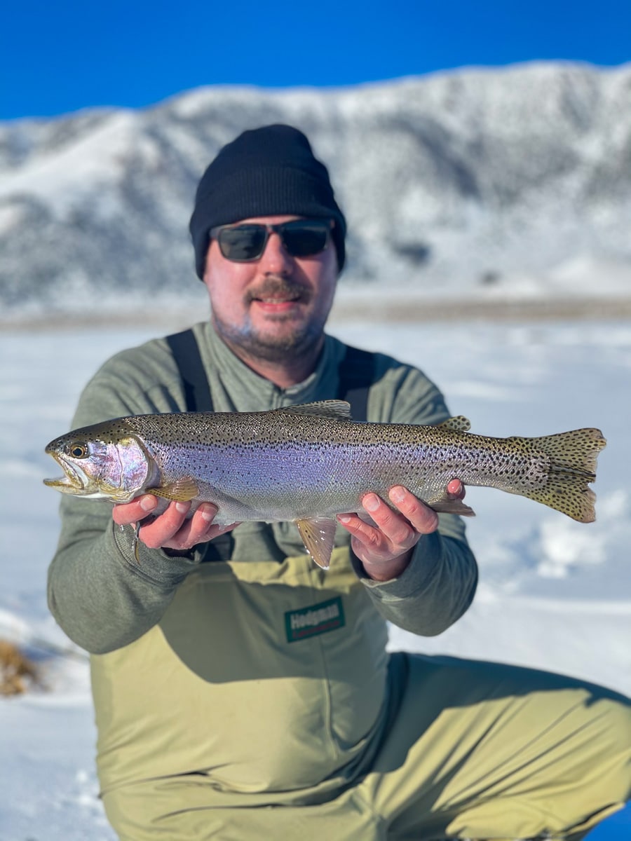 A fly fisherman holding a rainbow trout in spawning colors from the Upper Owens River in the snow.