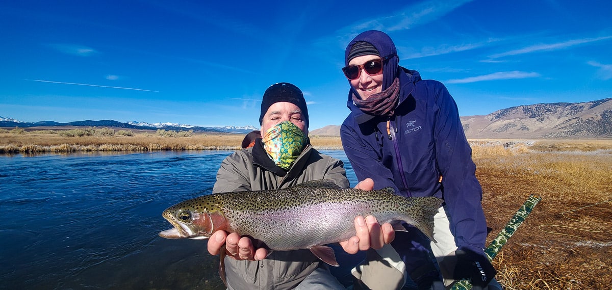 A masked fly fisherman holding a rainbow trout in spawning colors from the Upper Owens River.