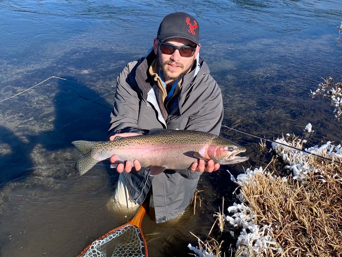 A masked fly fisherman holding a rainbow trout in spawning colors from the Upper Owens River.