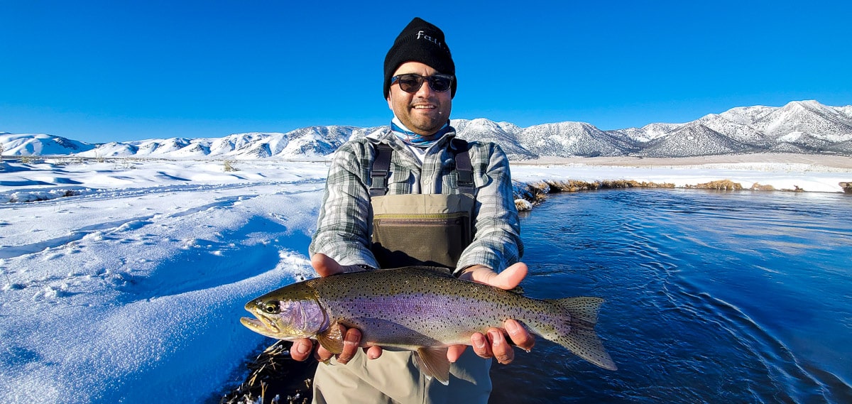 A masked fly fisherman holding a rainbow trout in spawning colors from the Upper Owens River.