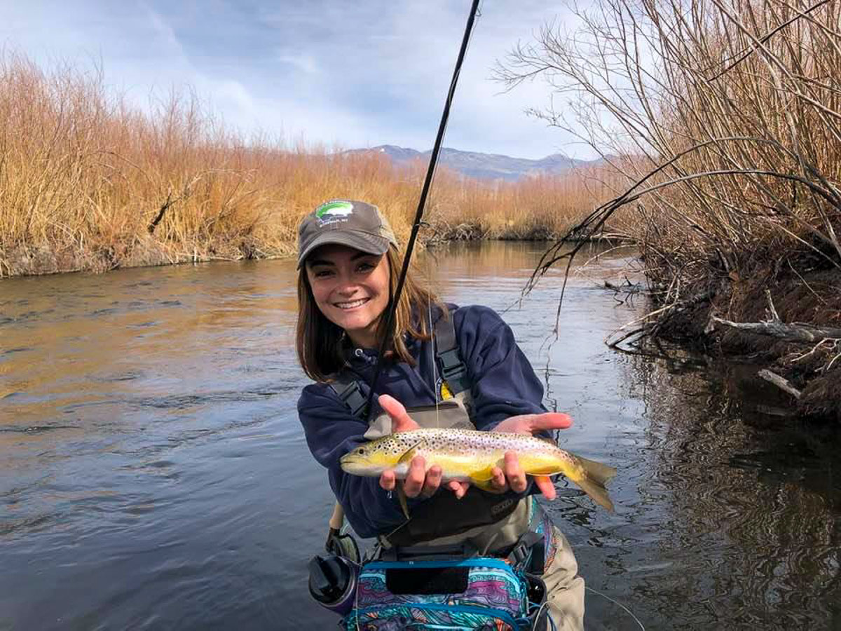 A fly fisherwoman holding a brown trout in spawning colors from the Lower Owens River.