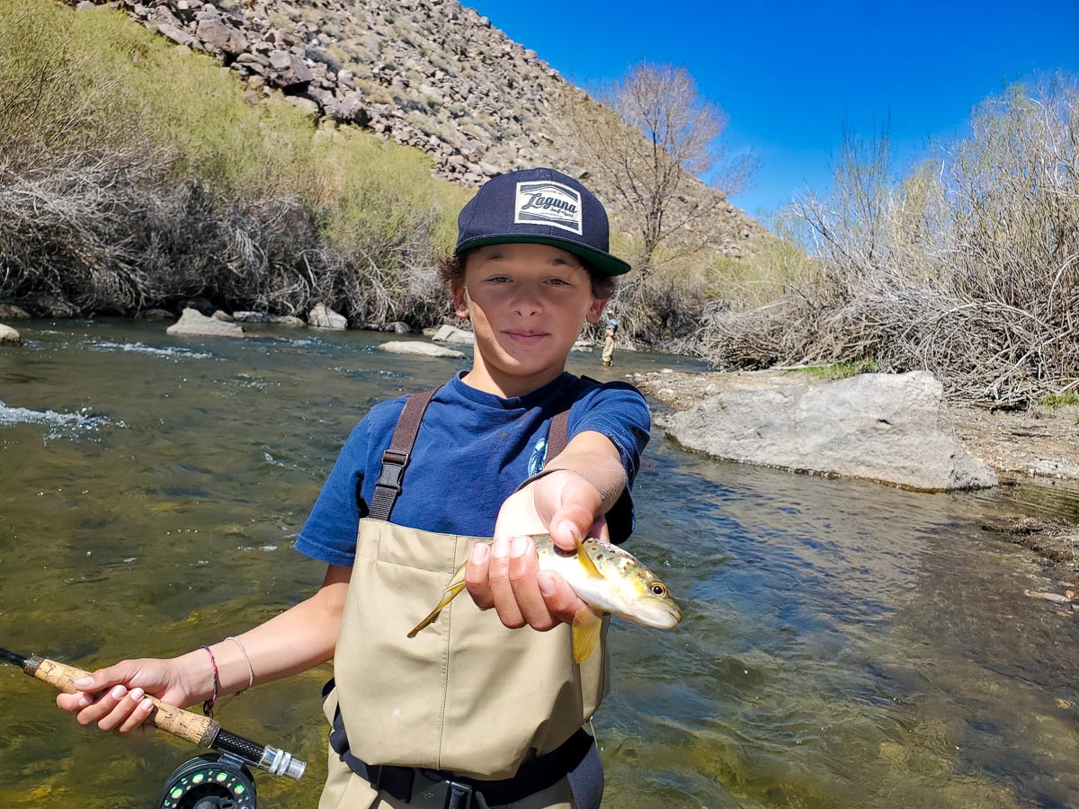 A fly fisherman youth holding a rainbow trout while standing in a river.