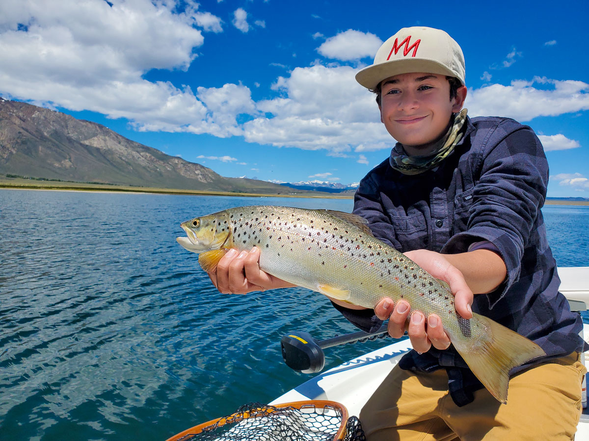 A young boy holding a brown trout on a lake.