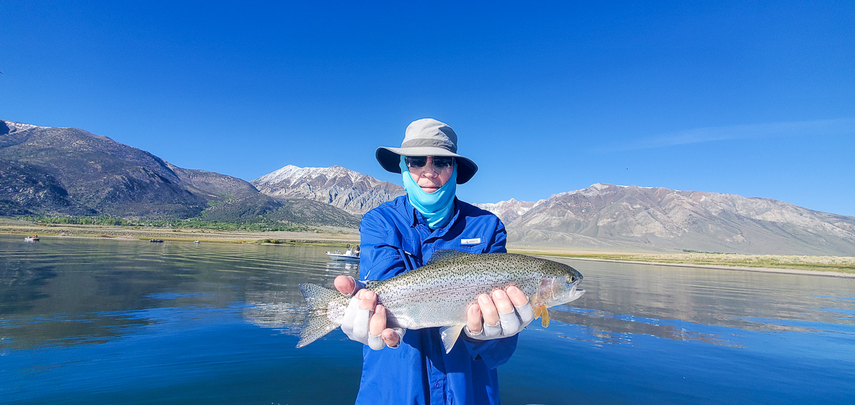 A man holding a large rainbow trout on a lake.