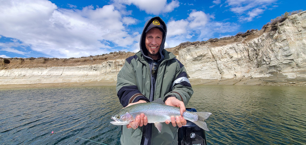 A hooded angler holding a rainbow trout on a mountain lake.