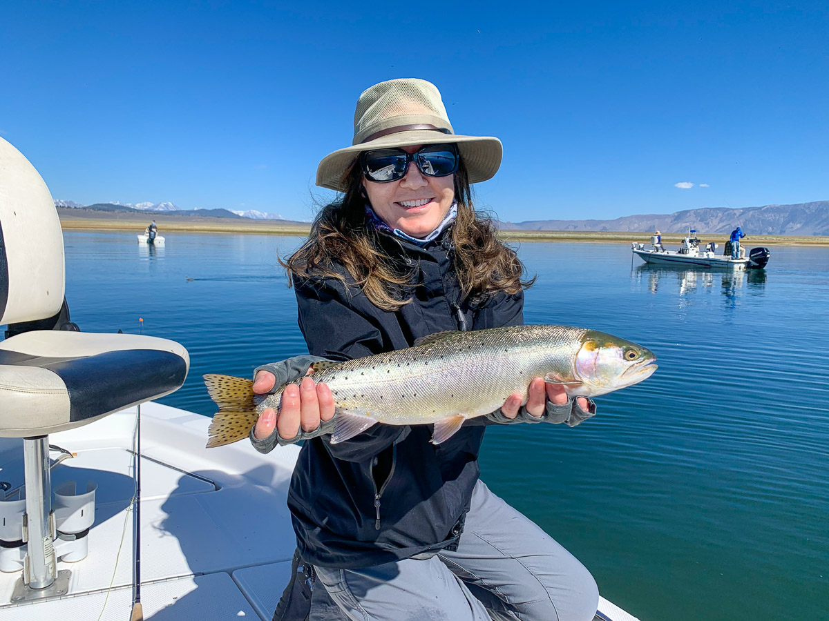 A female fly fisher holding a giant cutthroat trout in a boat on Crowley Lake.