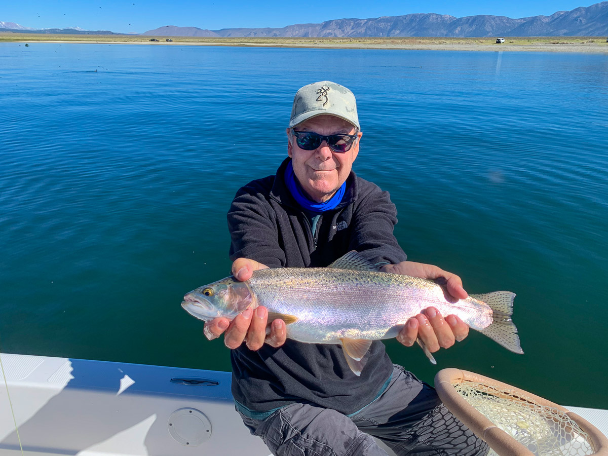 A man holding a large rainbow trout on a lake.