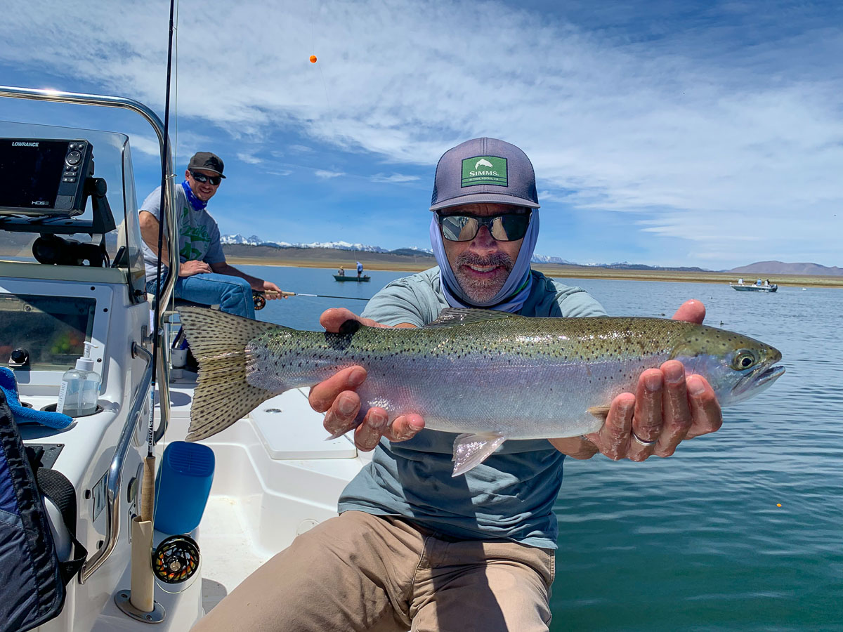A smiling angler with a purple hat holding a rainbow trout from Crowley Lake.